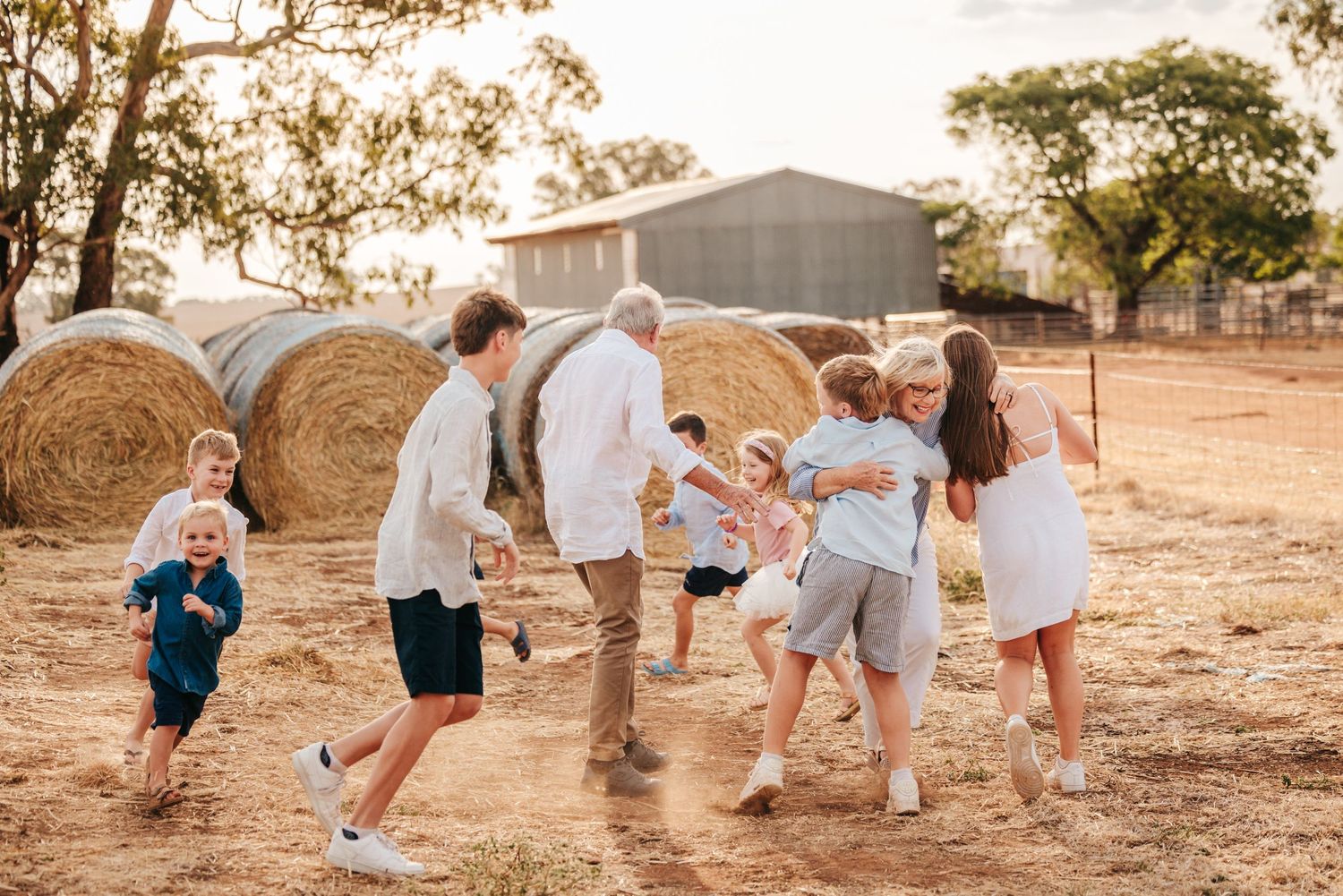 Group of people running and playing together near hay bales at sunset.