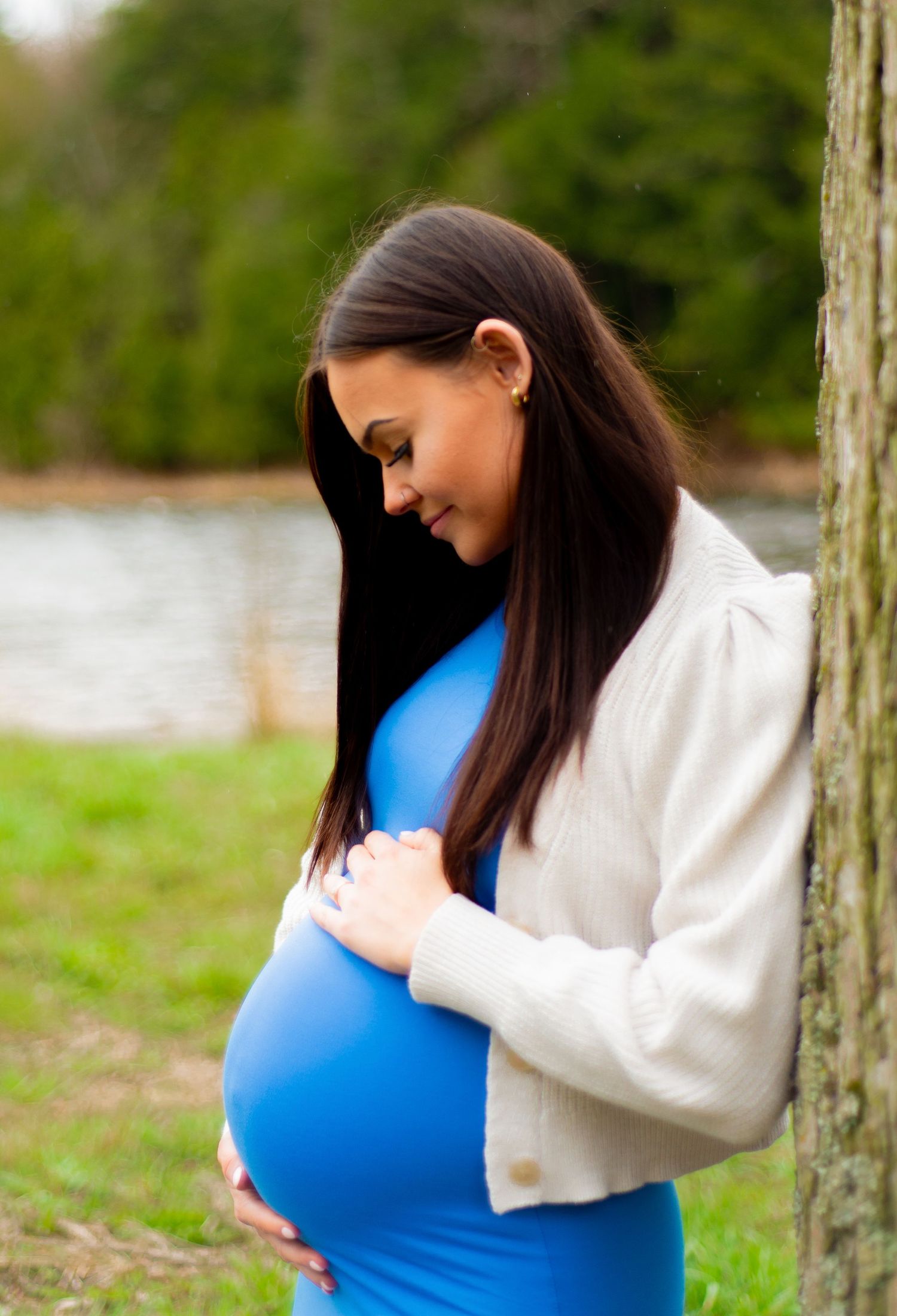 A maternal portrait of a woman in blue dress tenderly touching her baby bump.