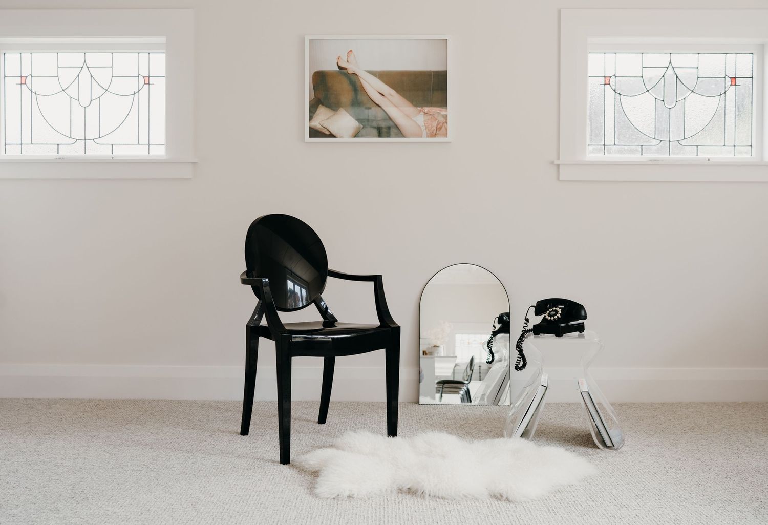 Minimal room setup with black and clear chairs against white walls with decorative windows.