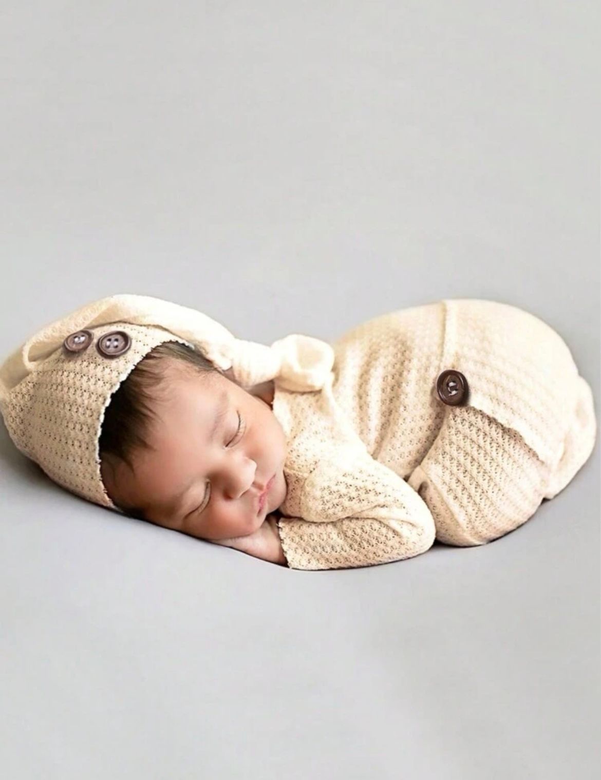 Sleeping newborn in cream knit romper on light grey background.