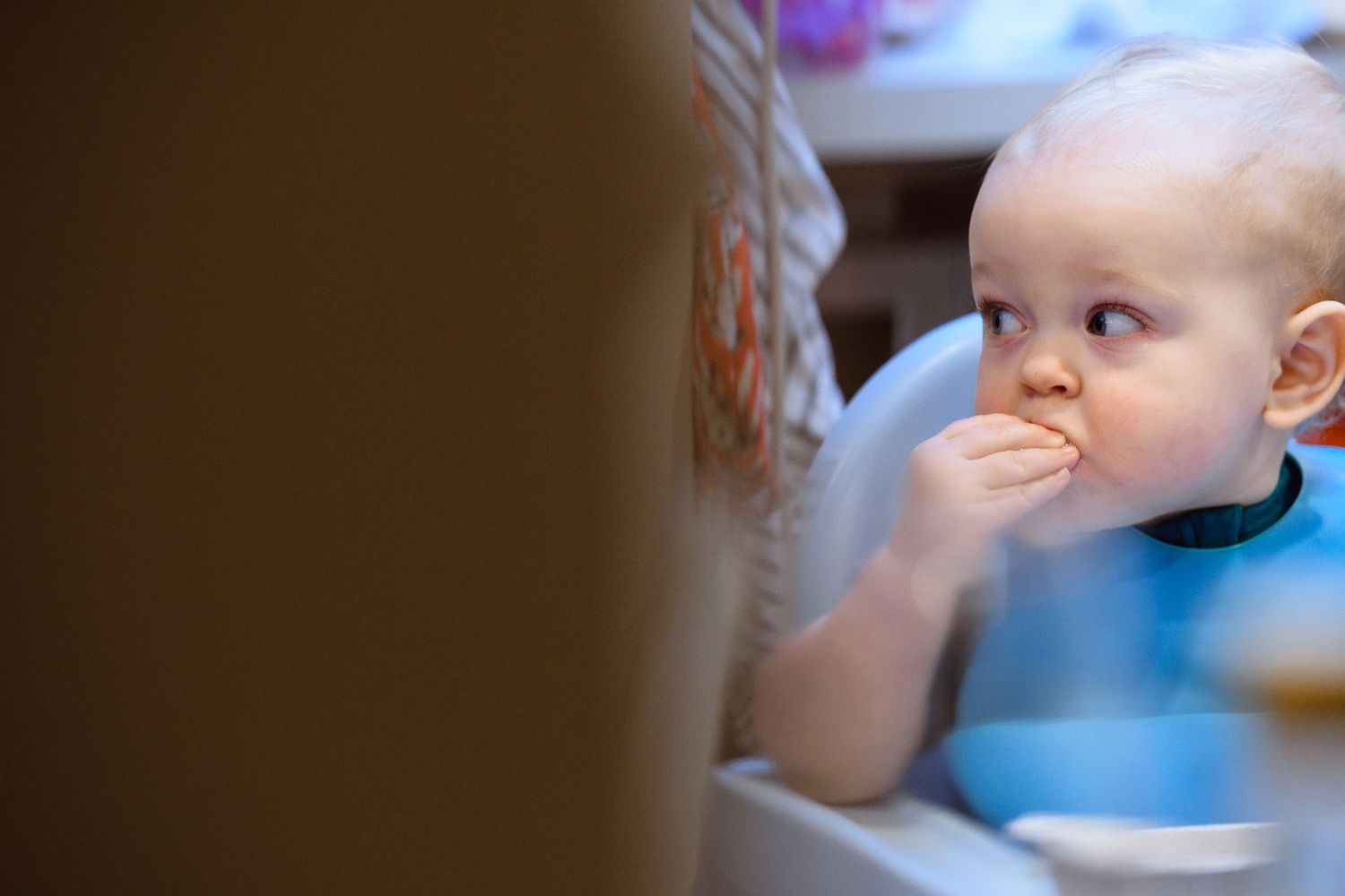 Baby in blue bib taking a bite of food during mealtime.