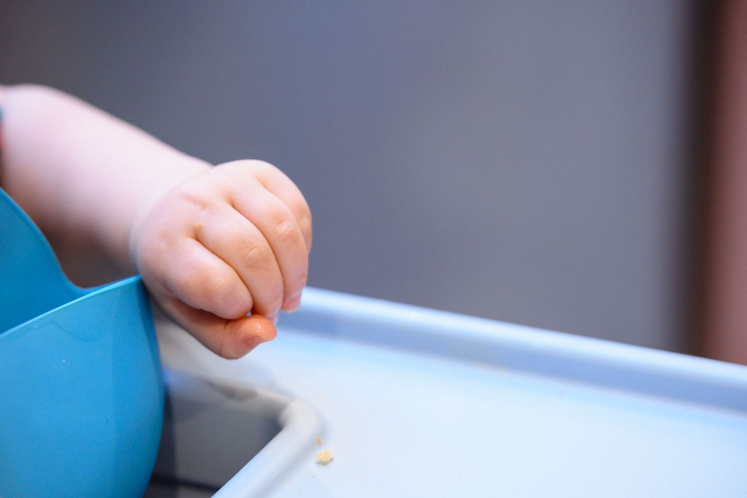 Close up view of small hand gripping edge of blue high chair tray.