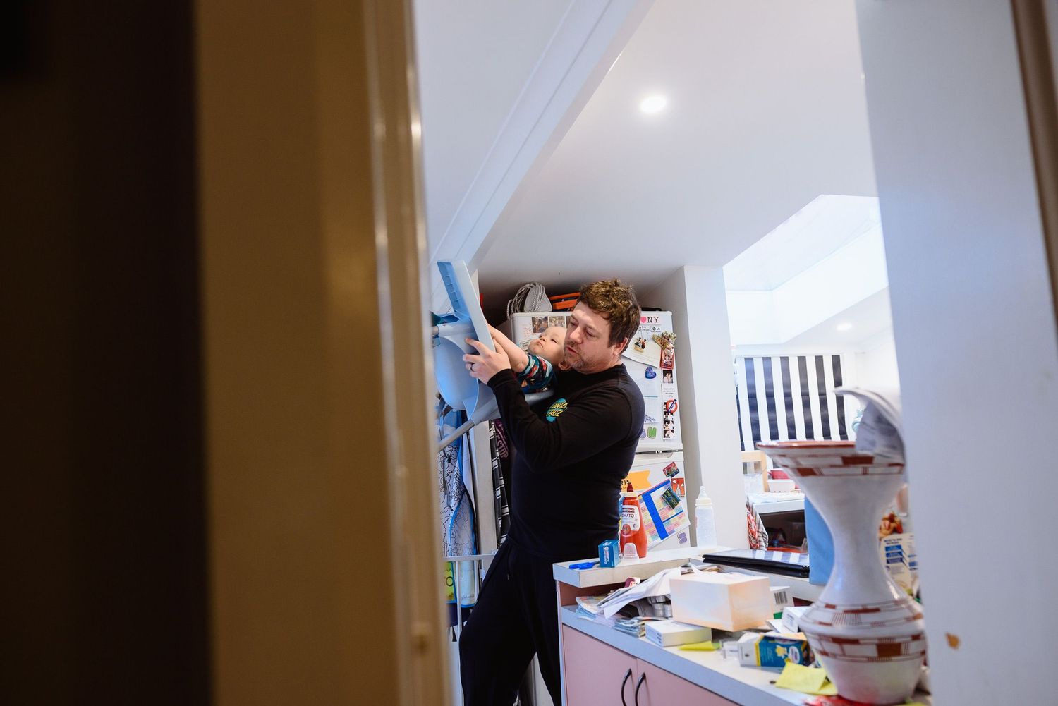 View through doorframe of person in kitchen wearing black clothing.