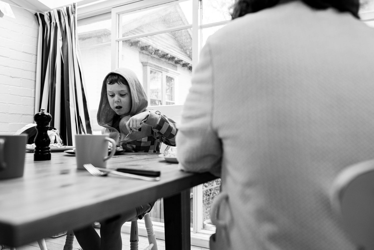 Black and white image of dining table scene with striped curtains in background.
