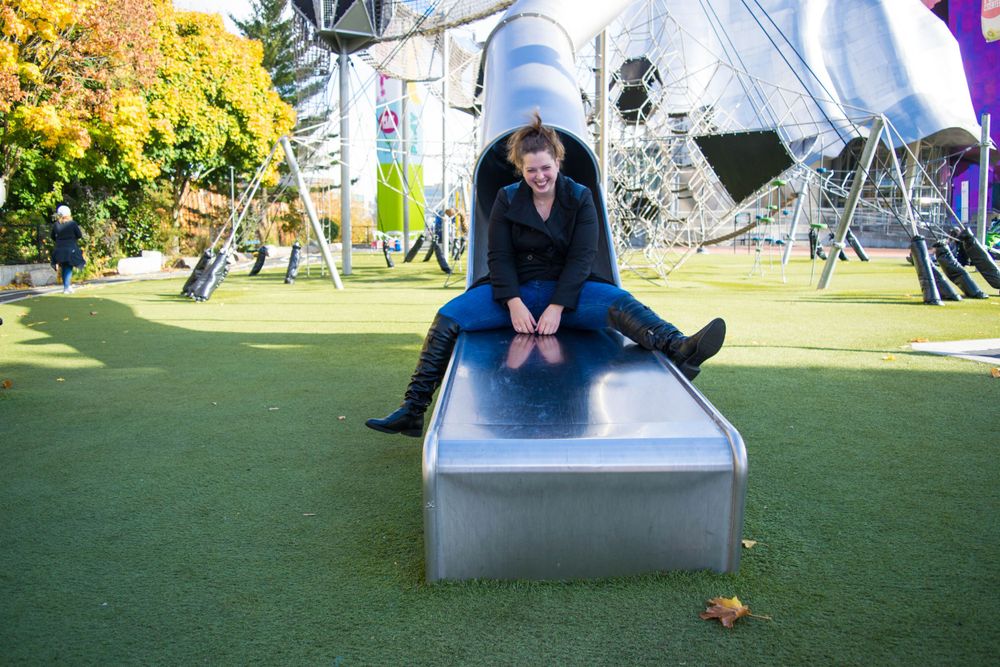 Person sitting on a metallic sculpture in an outdoor art installation space.