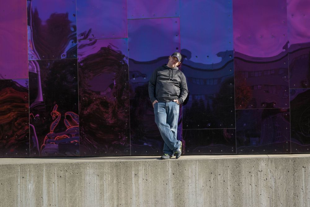 Person standing against a colorful purple wall with mountains in the background at sunset.