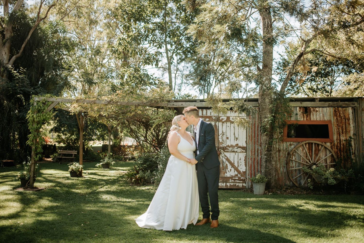 A couple embraces on their wedding day in front of a rustic barn door in a garden setting.