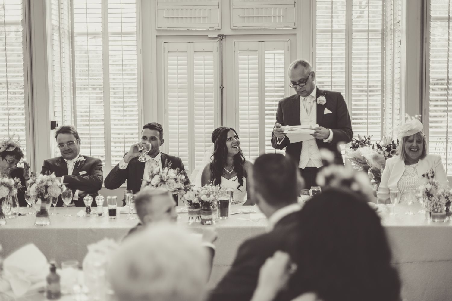 Wedding reception dinner with guests gathered at long tables in an elegant white room.