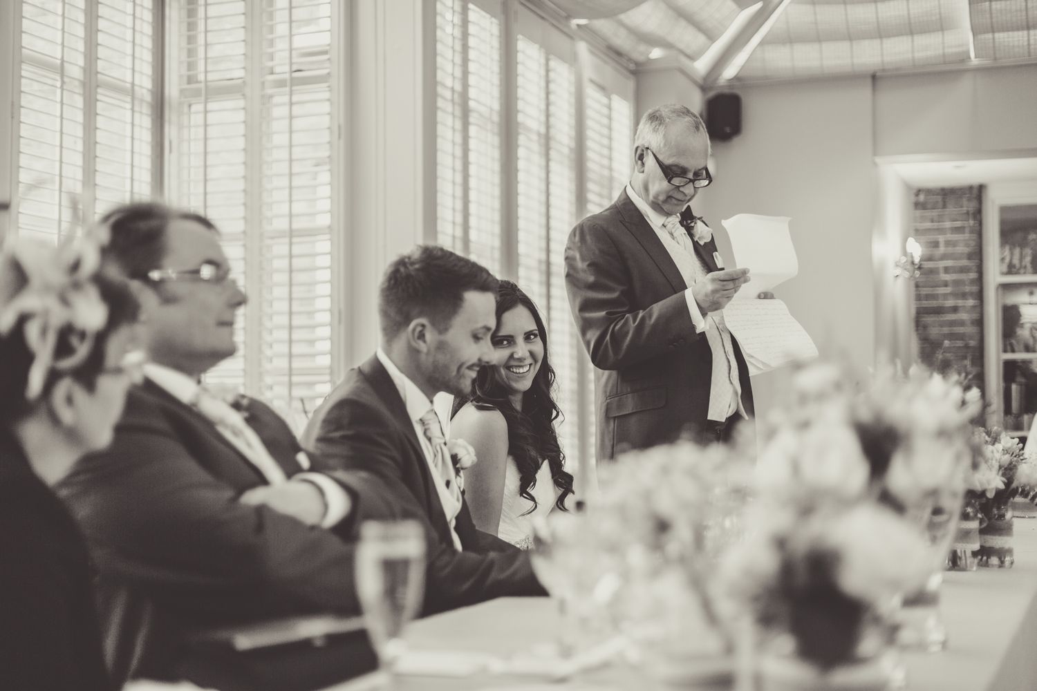 Vintage style photograph of wedding guests enjoying speeches at reception dinner.