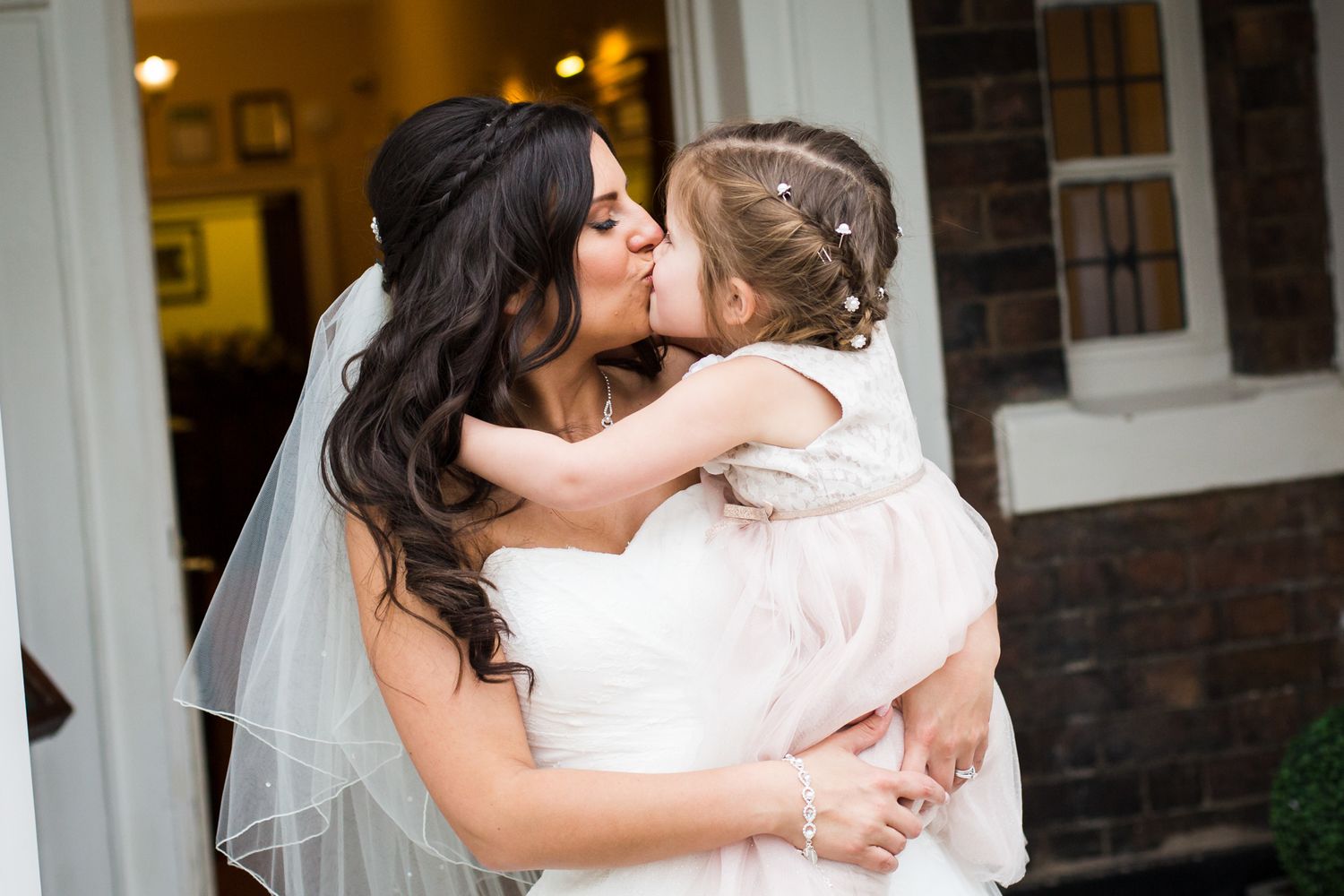 Tender moment between bride and young child at elegant brick venue entrance.