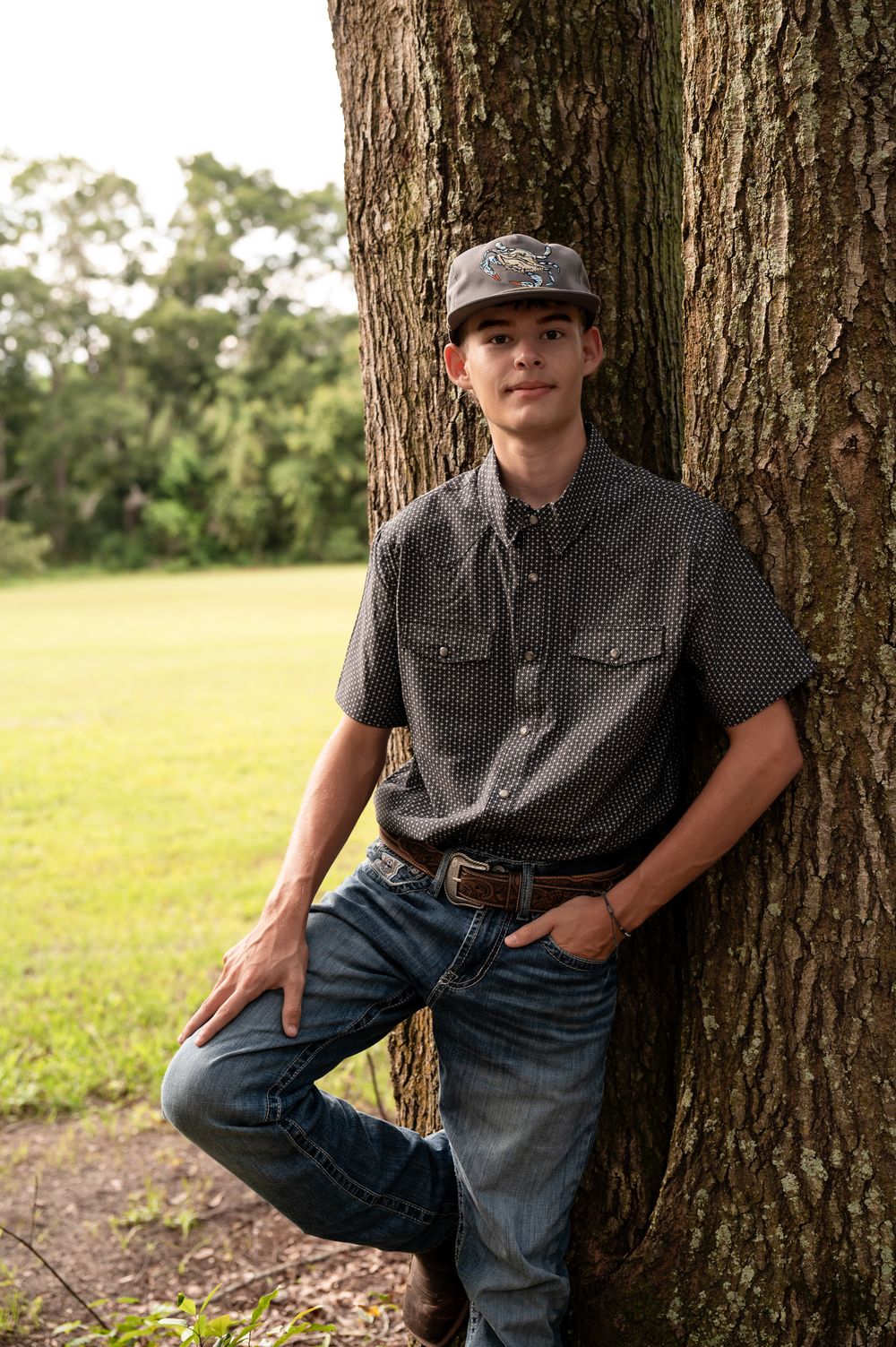 Casual outdoor portrait series showing someone leaning against a large tree trunk in a grassy field.