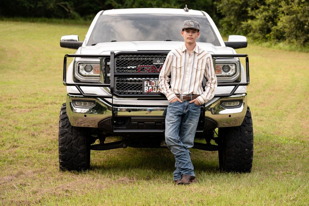 A lifted white GMC Sierra truck sits on a grassy field with its chrome front grille and wheels prominently displayed.
