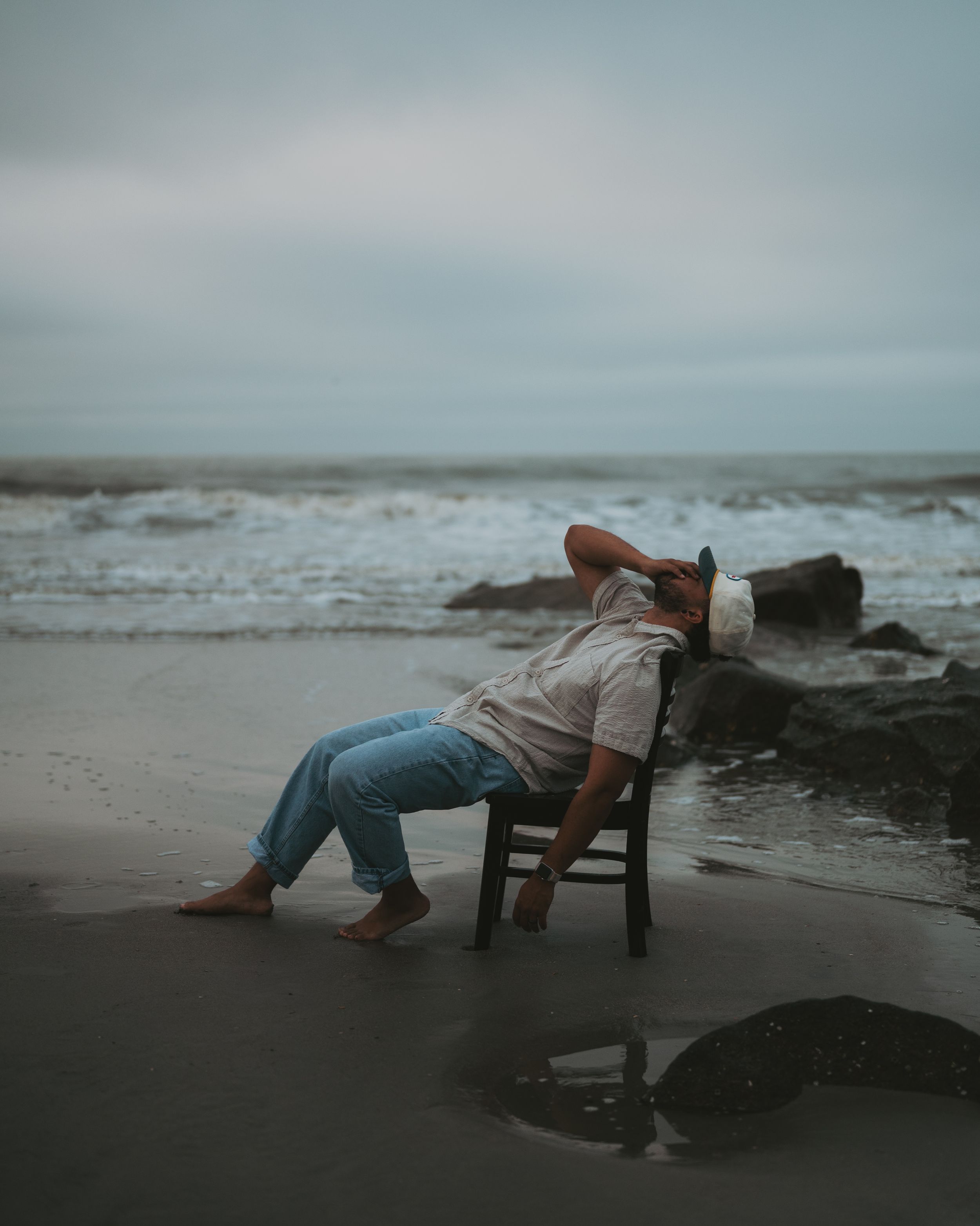 Person relaxing in wooden chair on moody beach with crashing waves in background.