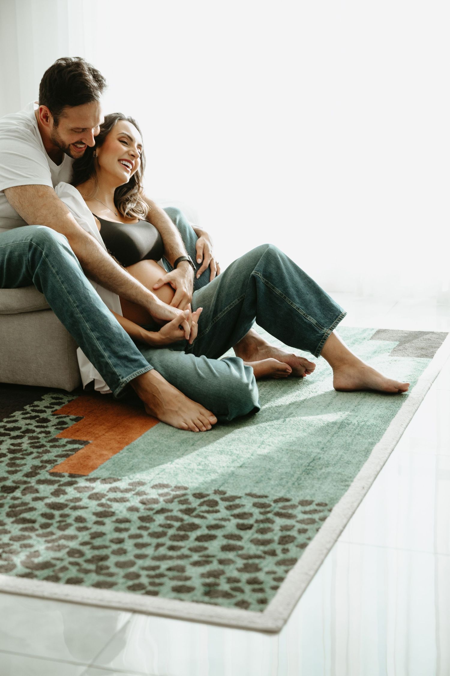 Intimate maternity photo of couple embracing on floor in natural light.