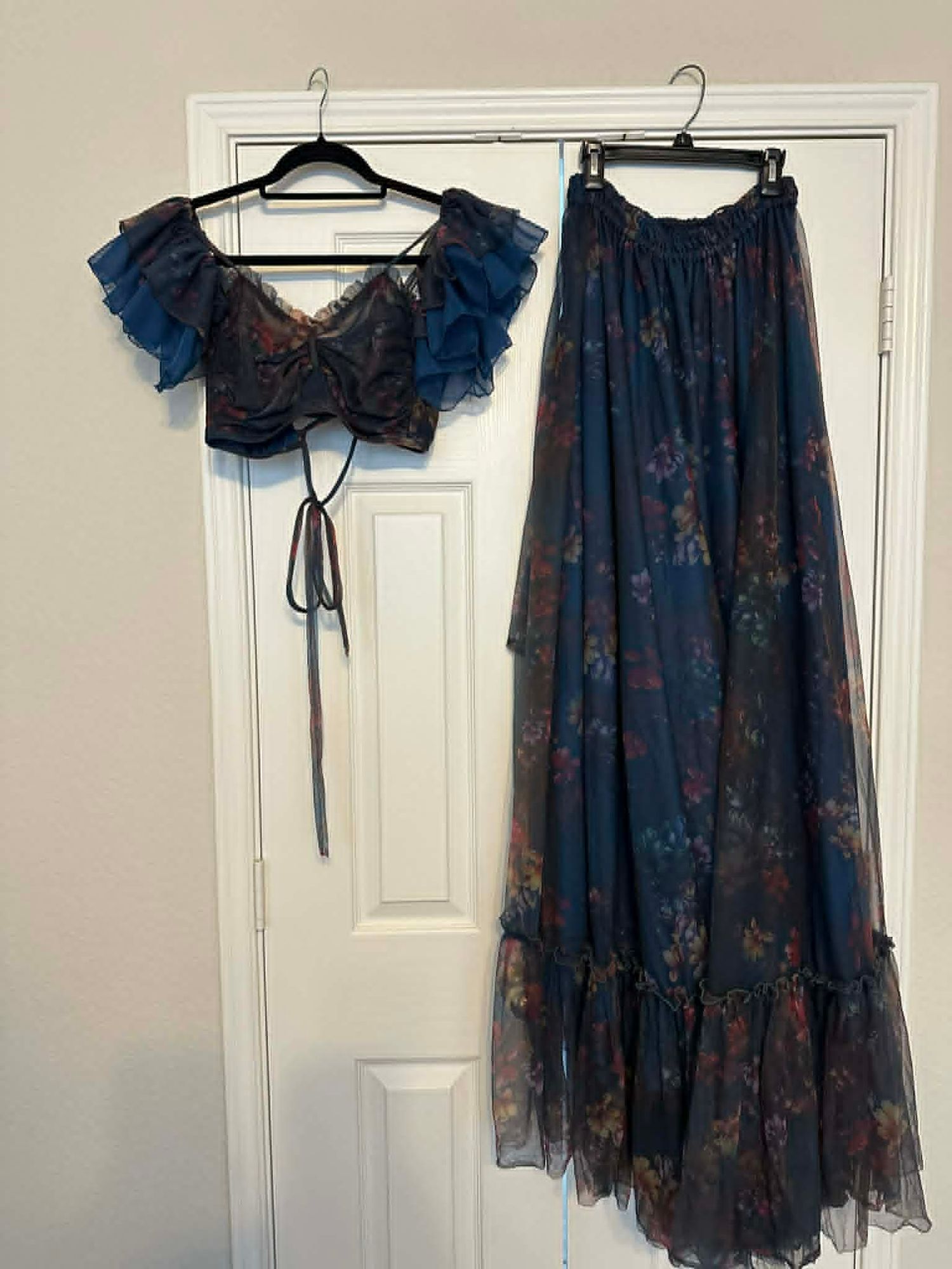 Blue floral two-piece set with ruffled crop top and maxi skirt, displayed on hangers against a white door.