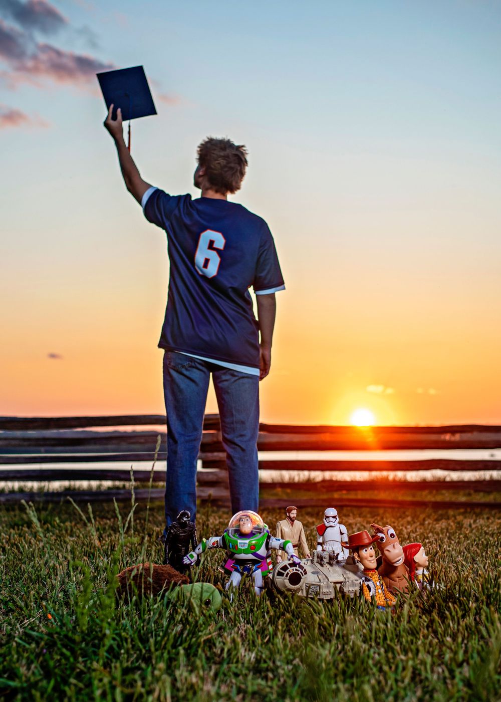 Teen in jersey #6 holds diploma at sunset with childhood toys at feet, celebrating graduation milestone.