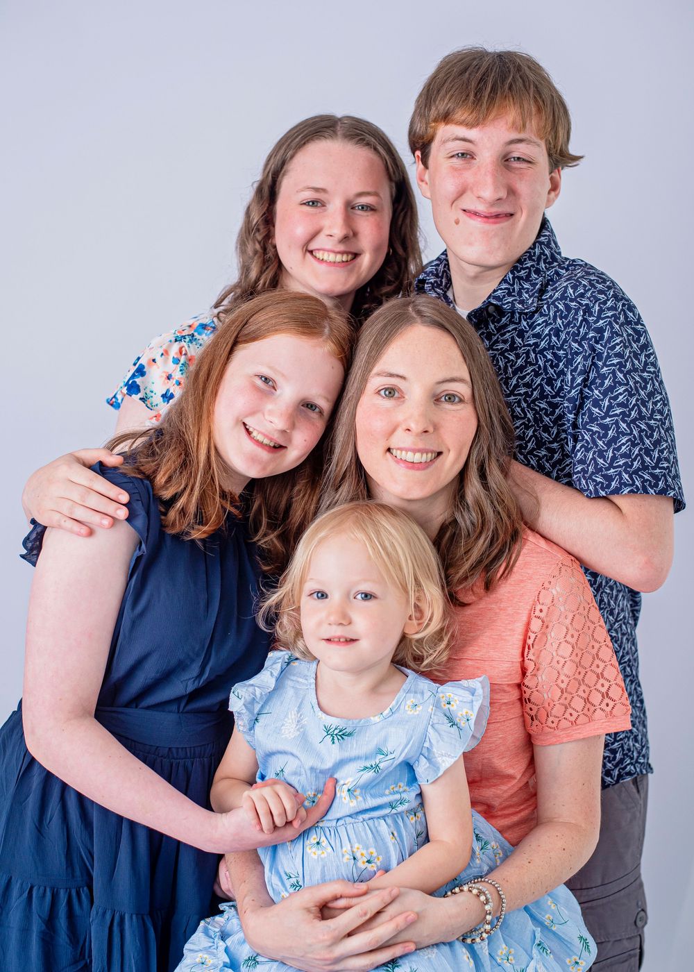 A smiling family of five poses together in a studio portrait, including a mother and four children of varying ages.