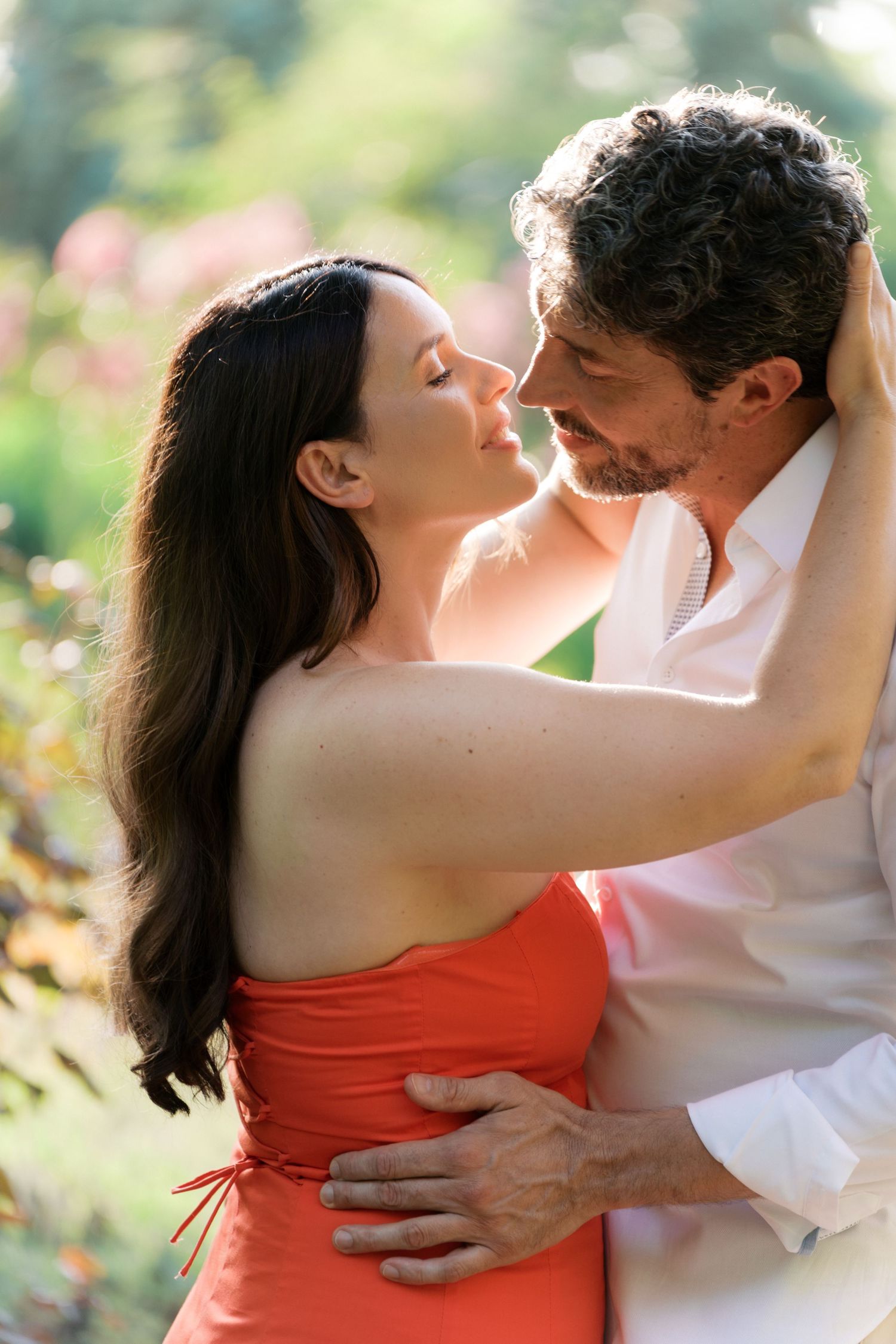 Intimate embrace captured from behind with long flowing hair against natural green backdrop.