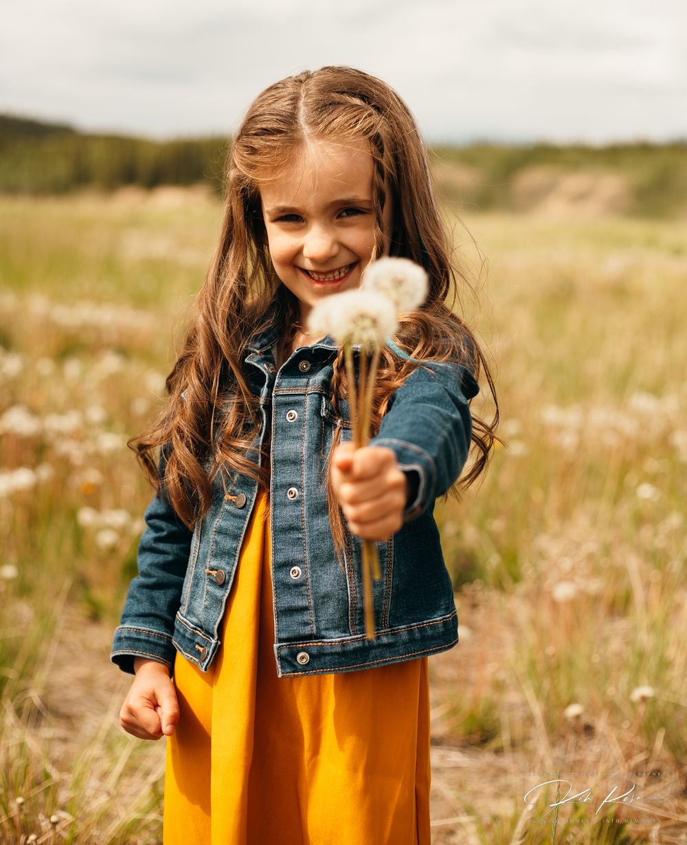 Smiling girl in yellow dress holding dandelions in a sunny wildflower field.