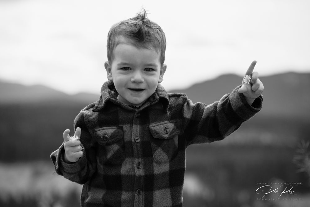 Black and white photo of a playful young boy giving thumbs up outdoors.