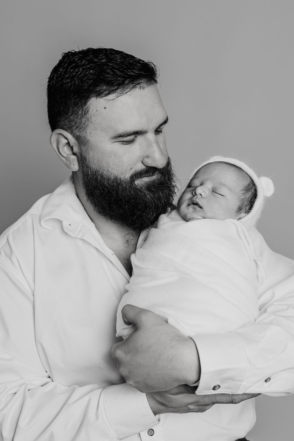 Black and white portrait of parent holding sleeping newborn wrapped in white blanket.