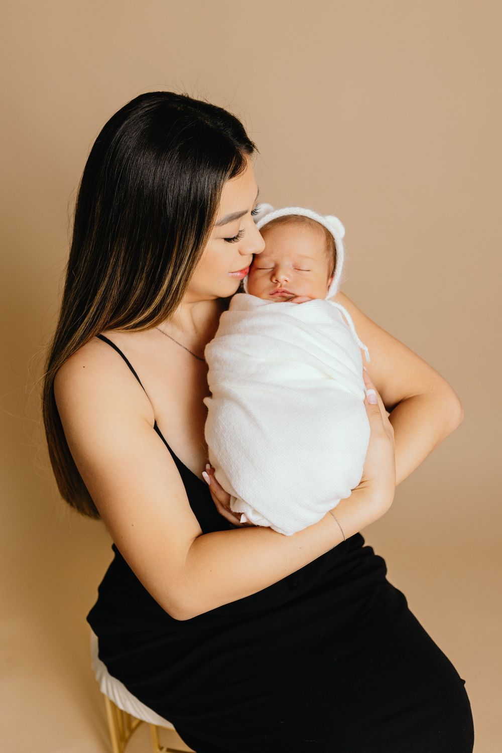 Intimate portrait of parent tenderly kissing sleeping newborn swaddled in white.