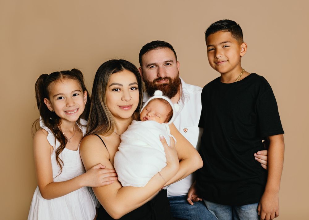 Studio family portrait with newborn baby against beige background.