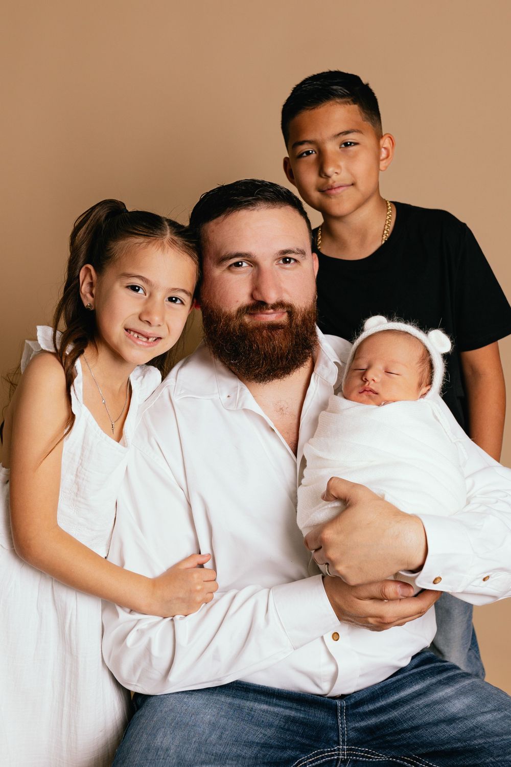 Studio portrait of family members with newborn baby against warm beige backdrop.