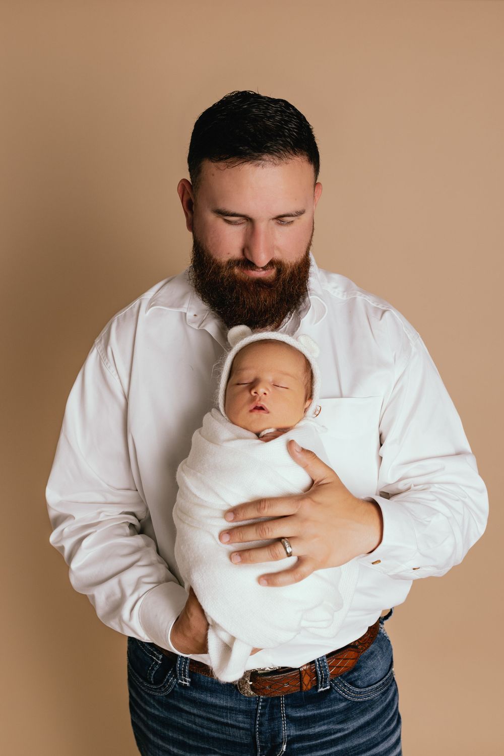 A tender moment between parent and newborn baby swaddled in white against a neutral background.