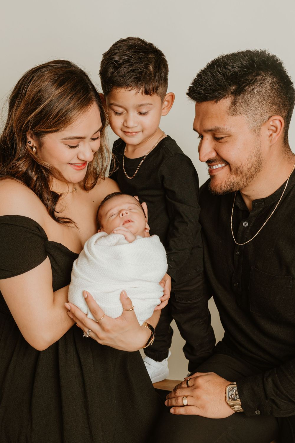 Intimate family portrait in black attire against neutral background.