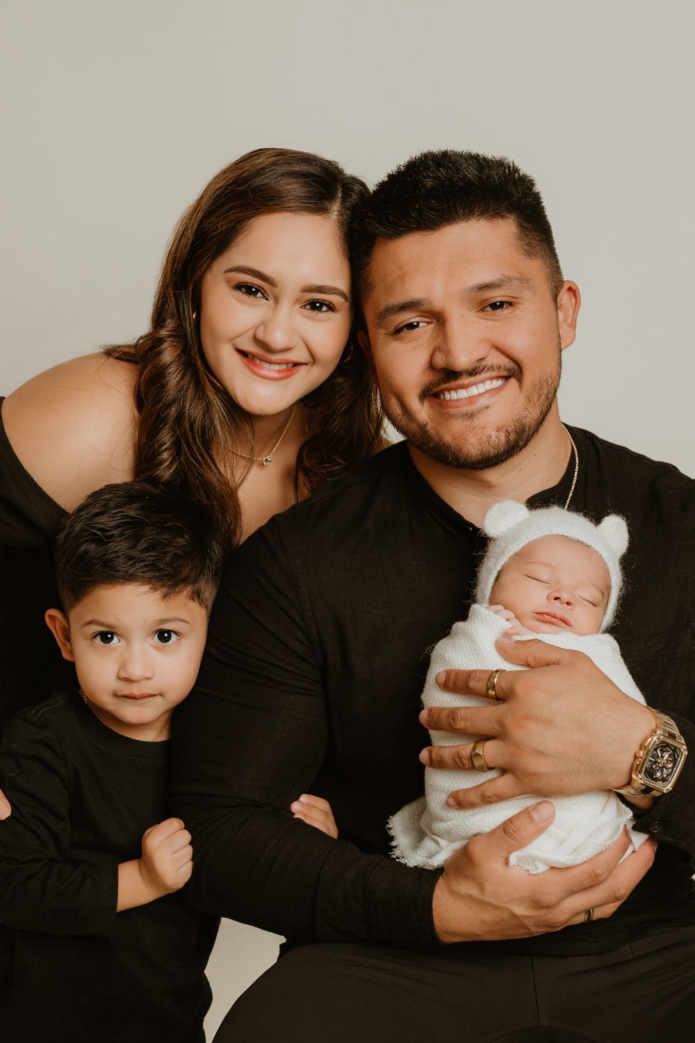 Family portrait against neutral backdrop showing parents with their children in coordinated black outfits.