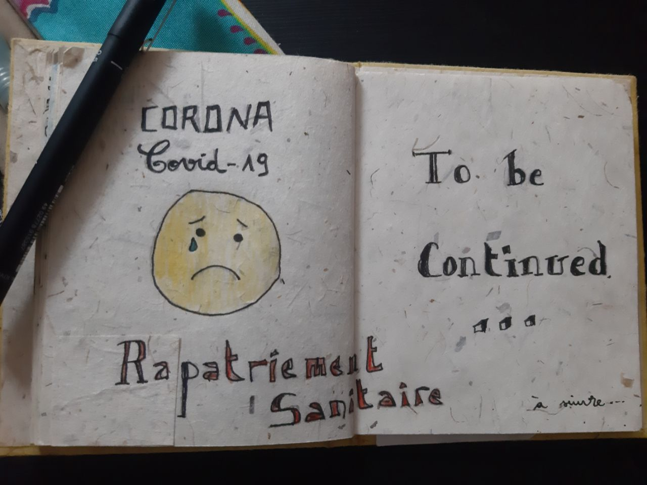 Hand-drawn sad face with text about Corona COVID-19 in a notebook.