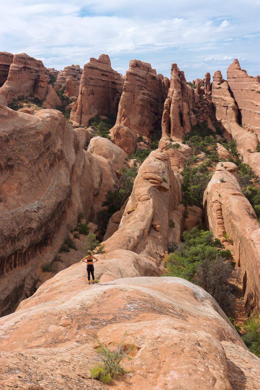 landscape image of rock formation fins in moab utah with girl hiking over top