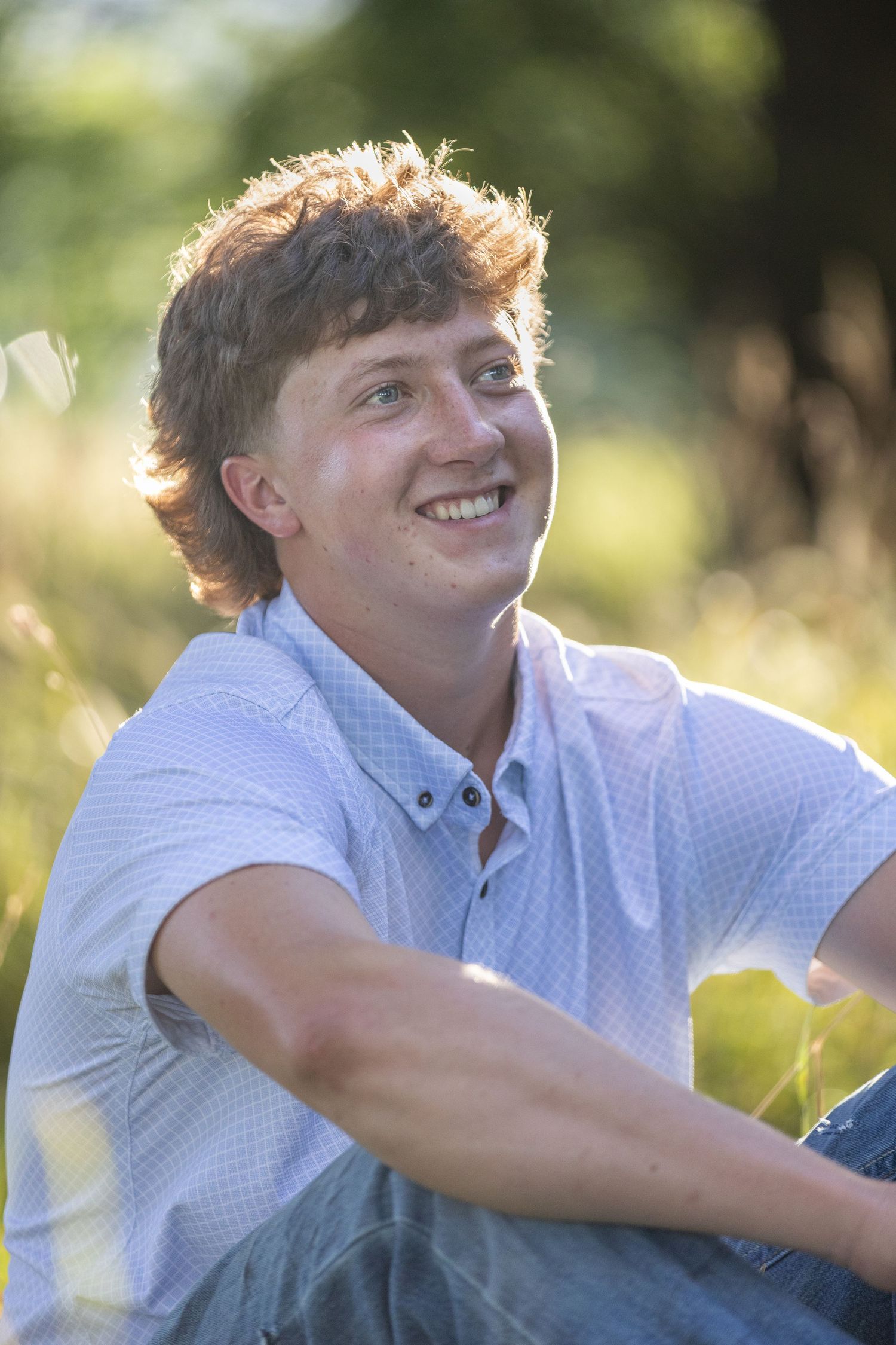 A student relaxes outdoors on a sunny day while wearing a white polka dot shirt and backlit by natural lighting.