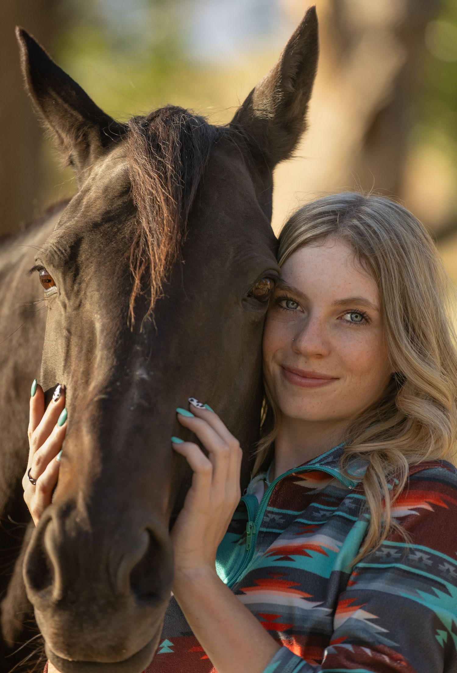 A woman in a turquoise and red plaid shirt shares a tender moment with a dark brown horse outdoors.