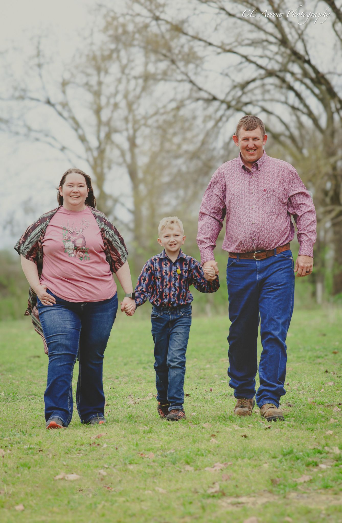 Family of three walking hand in hand through grassy field on spring day.