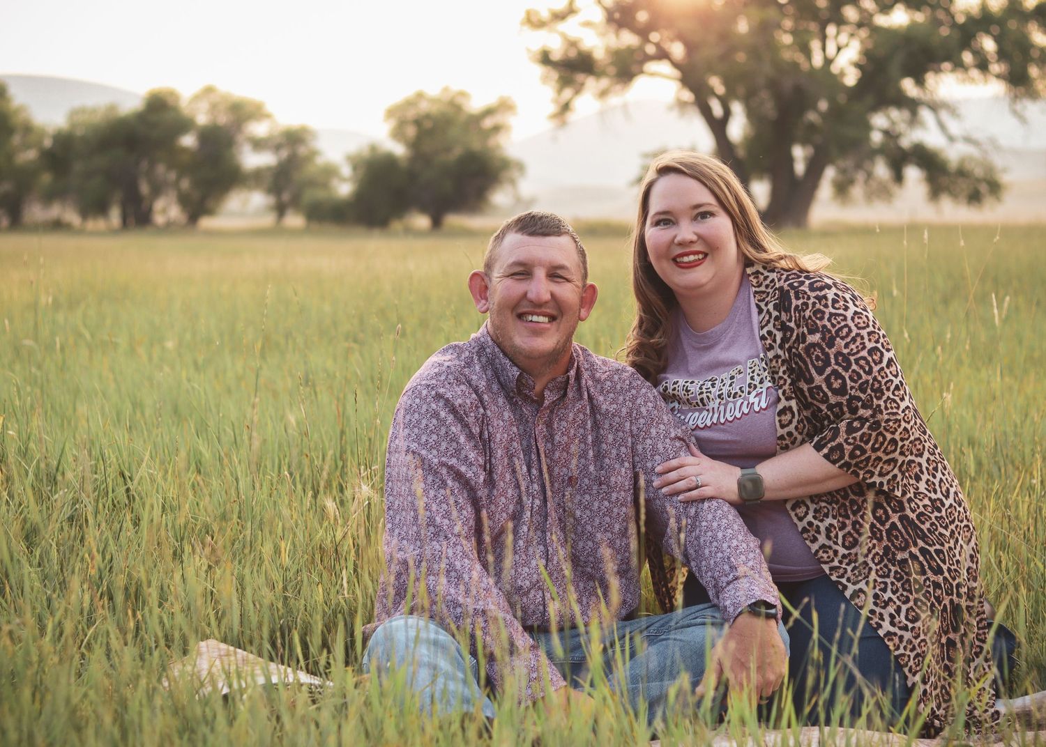 A couple sitting together in a tall grass field during golden hour.