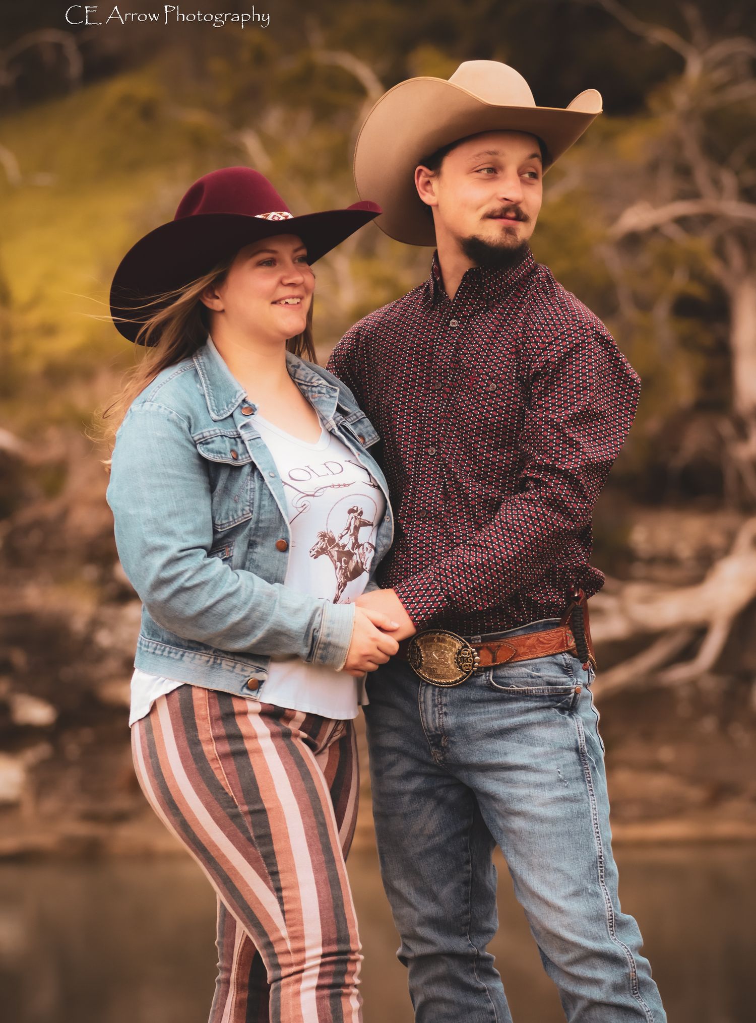 Country western couple in cowboy hats and casual attire pose outdoors.