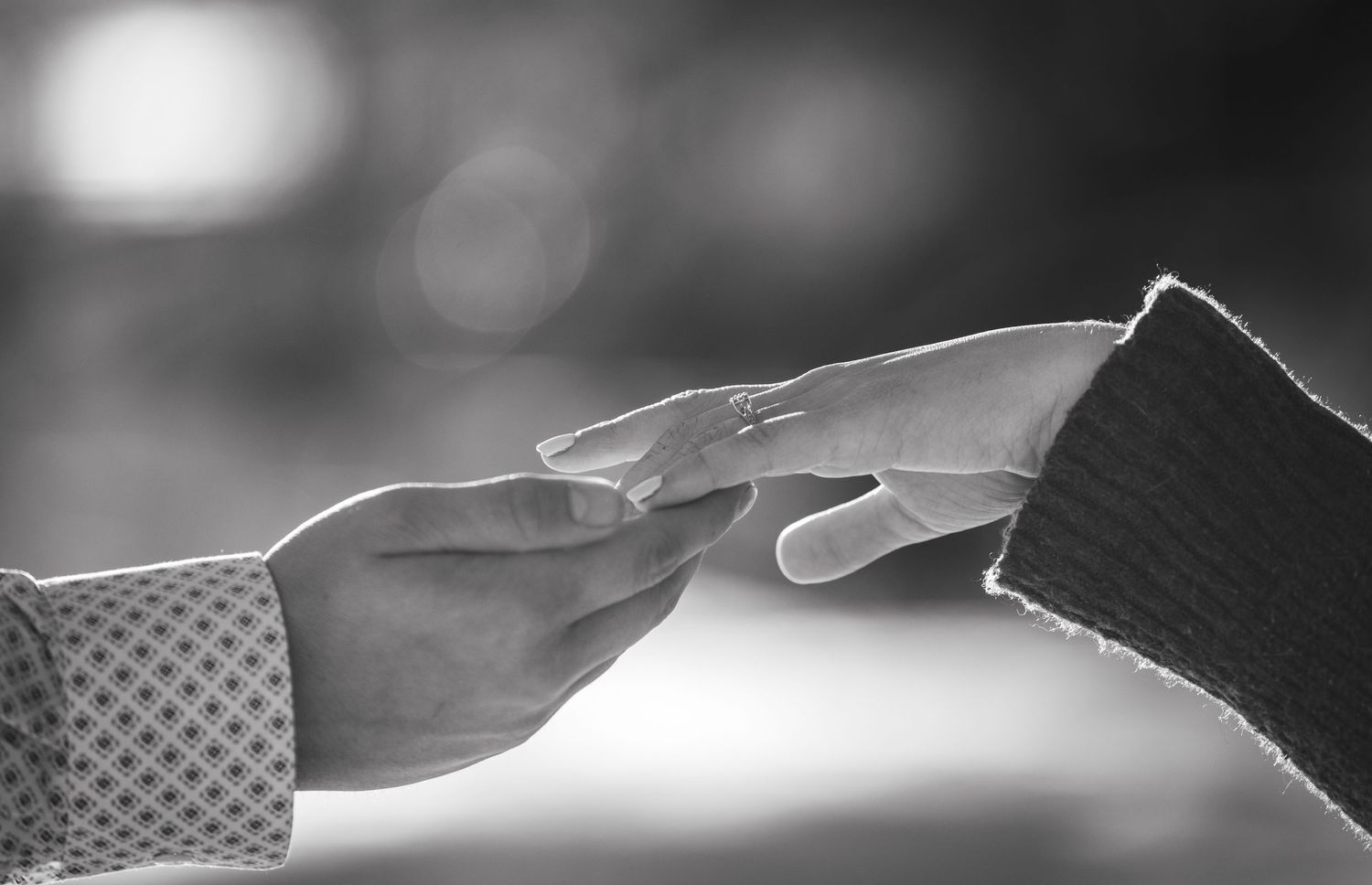 Two hands reaching towards each other in a tender moment, captured in black and white with soft bokeh lighting.