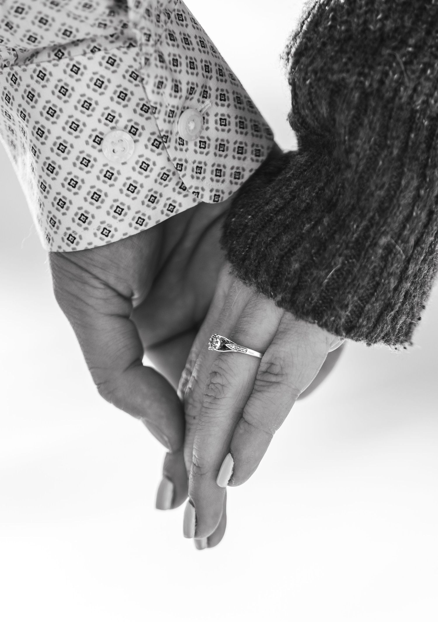 Black and white image of two people holding hands, with one wearing a patterned sleeve and a ring.