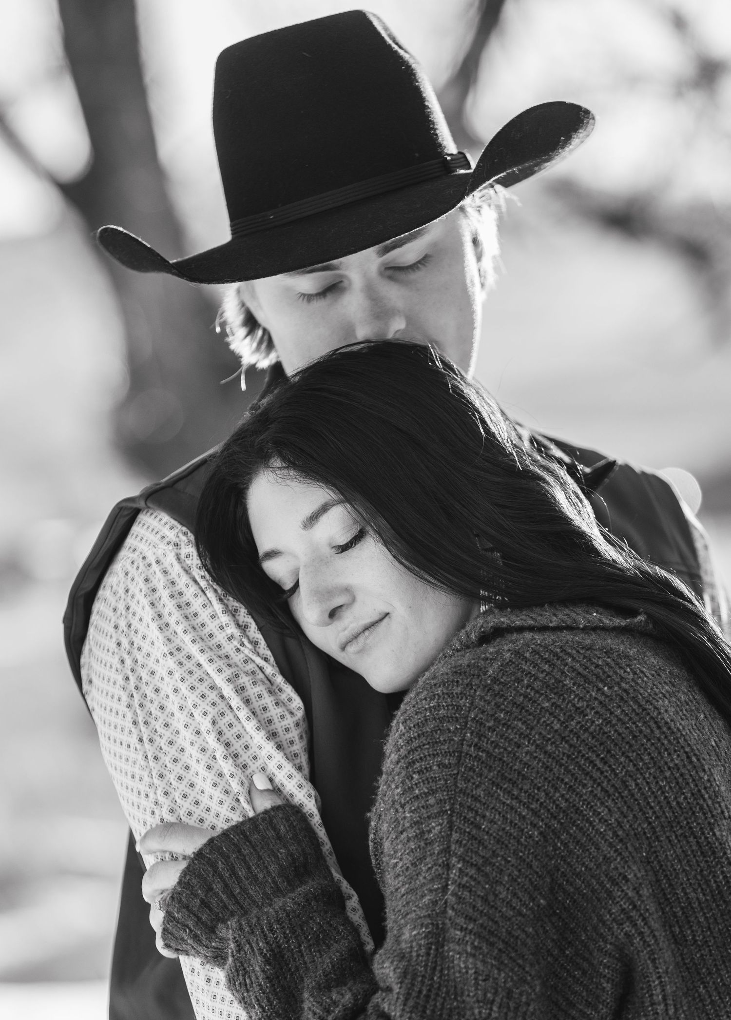 Black and white romantic portrait of a couple embracing, with one wearing a cowboy hat and sweater in an intimate moment.