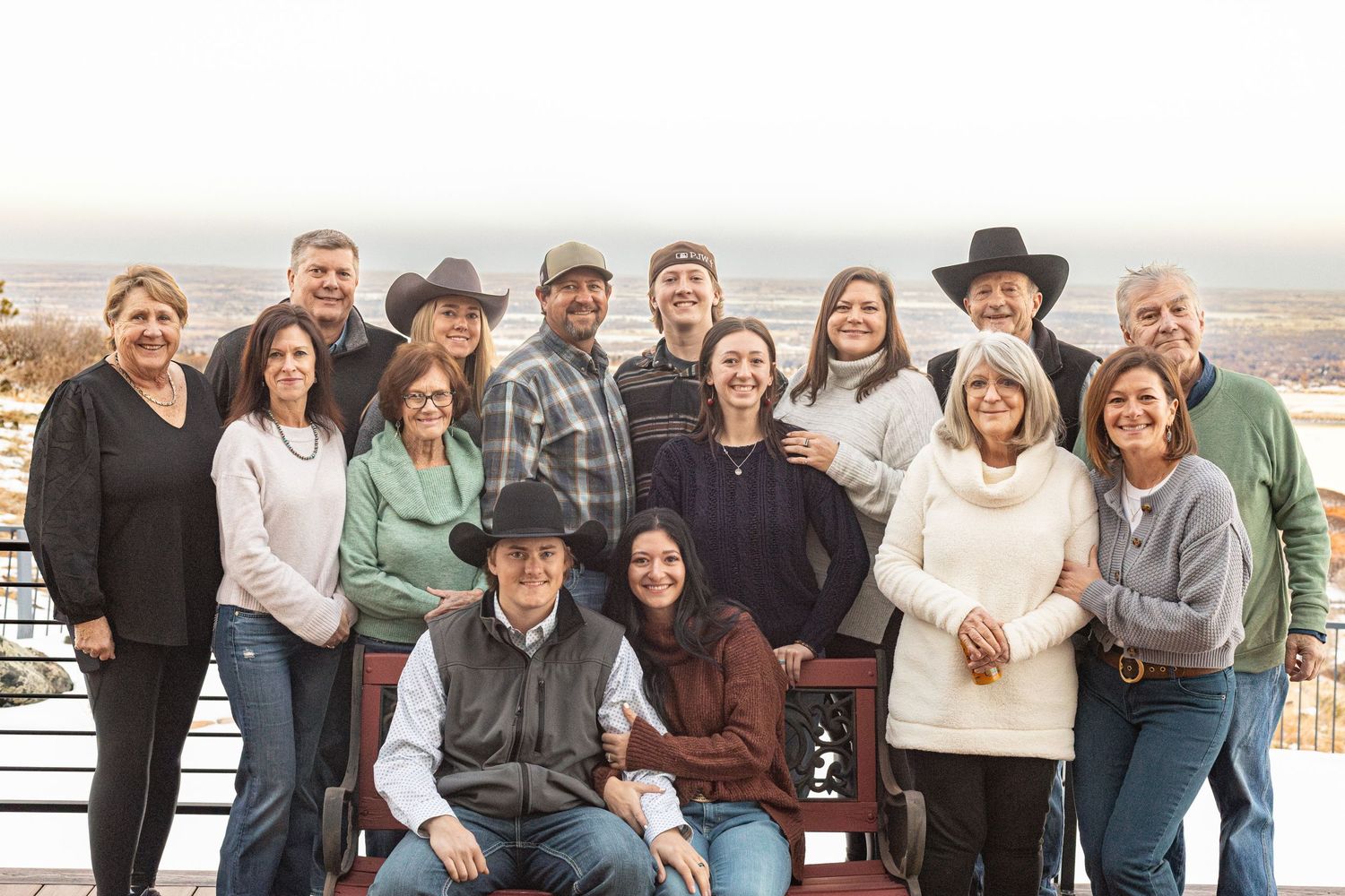 A large group wearing casual winter clothing poses together on an outdoor deck overlooking a desert landscape.