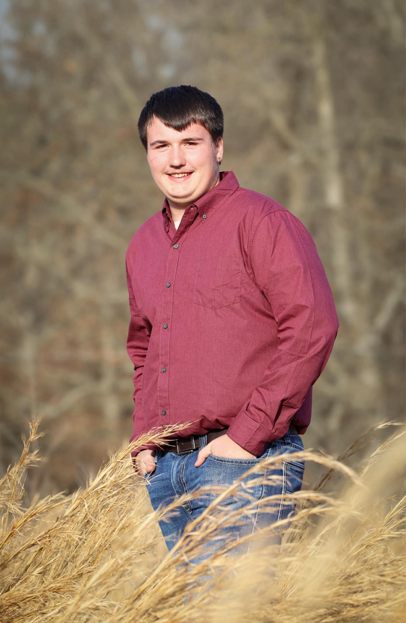 Portrait of someone in a burgundy button-down shirt standing in tall grass.