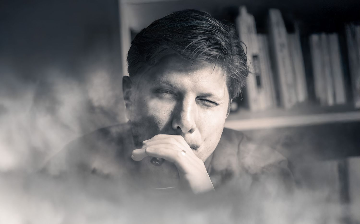 Grayscale portrait of a man in deep thought with a dreamy, fog-like overlay and bookshelves in the background.
