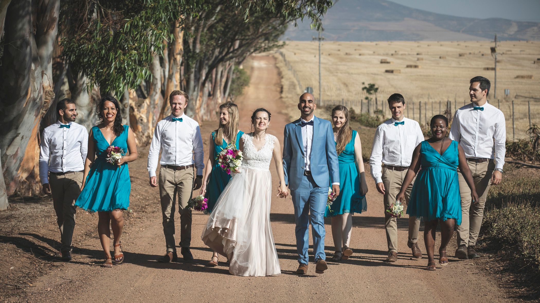 Baveer & Jess joyously walking down the road with their bridal party at Rondekuil Wedding Venue outside Durbanville, CT
