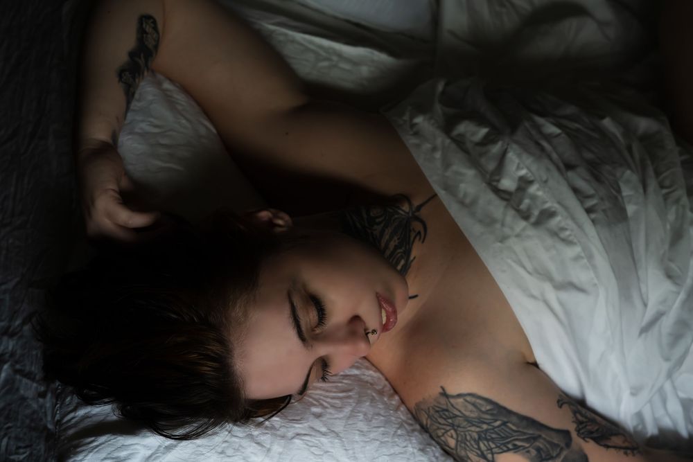 Person laying in bed under soft white sheets while sleeping peacefully in the dark.