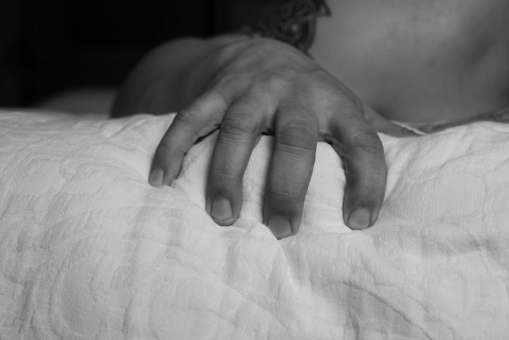 Close-up black and white image of hand grasping white bedsheets.