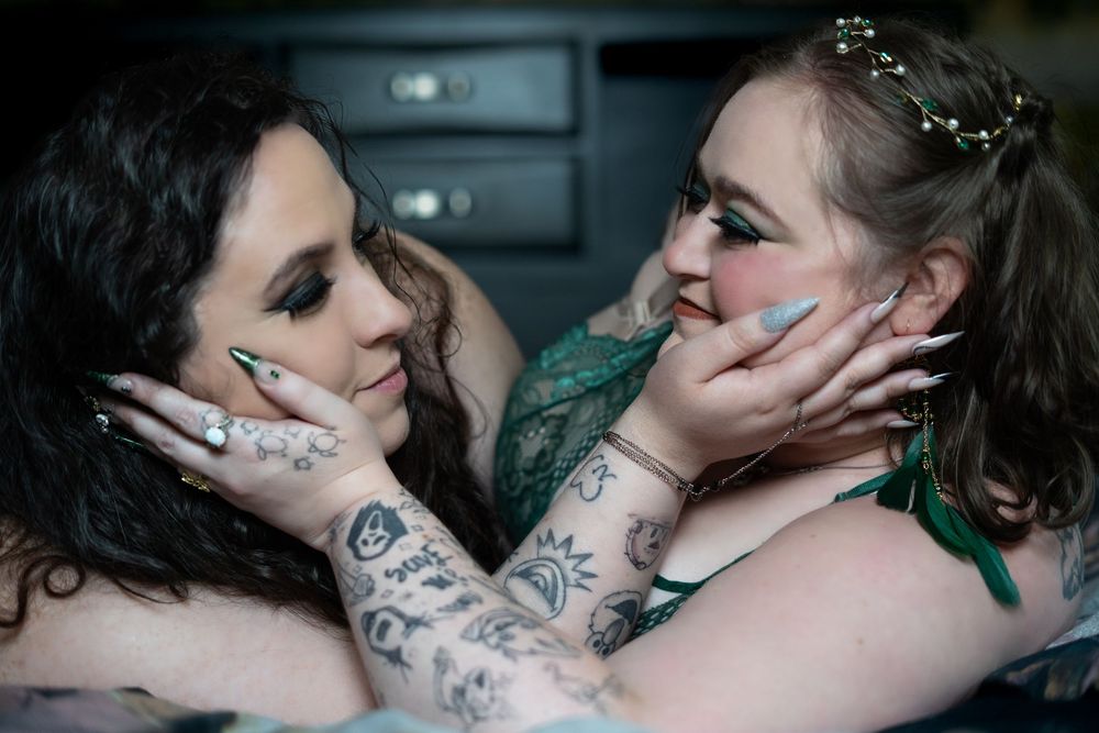 Two people embrace intimately in a dimly lit setting with dramatic lighting and shadows. LGBtQ couple, in boudoir portrait, Clarksburg WV