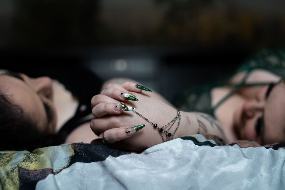 A close-up view of hands adorned with rings resting on light colored fabric in soft lighting. LGBTQ couple, Morgantown West Virginia