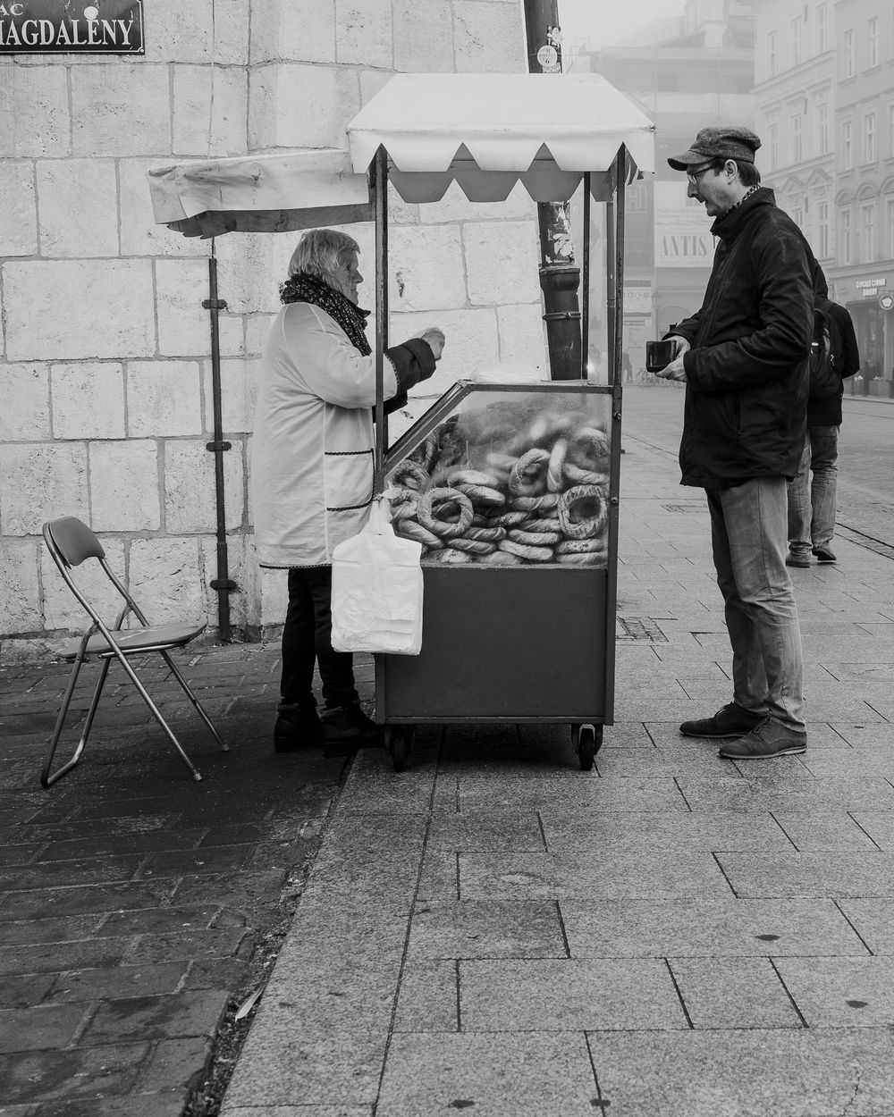 Black and white street scene of a vendor cart on cobblestone street.